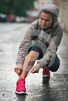 Fitness woman tying shoelaces outdoors in city