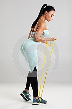 Fitness woman using a resistance band in her exercise routine. Sexy athletic girl workout with expander on gray background