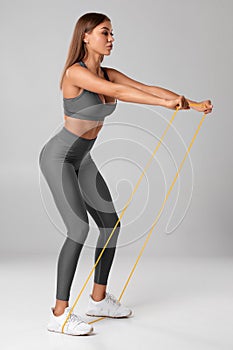 Fitness woman using a resistance band in her exercise routine. Sexy athletic girl workout with expander on gray background