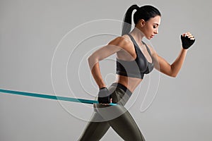 Fitness woman using a resistance band in her exercise. Sexy athletic girl workout with expander on grey background