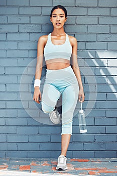 Fitness woman, water bottle and relax by city building wall in workout, training and exercise in Indonesia. Portrait