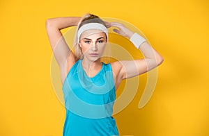 Fitness woman wears sportswear,sport clothing, posing and looking to side while keeps her arms over head, isolated on yellow