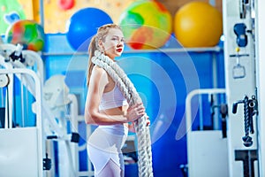 Fitness woman working out with battle rope at gym. posing on camera