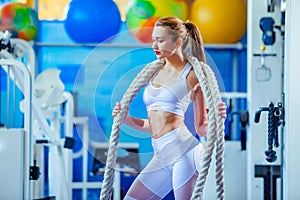 Fitness woman working out with battle rope at gym. posing on camera