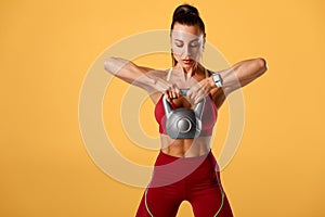 Fitness woman working out with kettlebell on orange background. Athletic girl doing exercise for delt