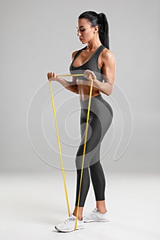 Fitness woman workout with resistance band isolated on gray background. Athletic girl doing exercise for biceps