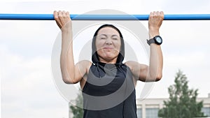 Fitness woman workout tries doing exercises on a horizontal bar outdoors