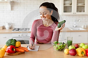 Fitness Woman Writing Down Healthy Recipes Holding Avocado At Kitchen