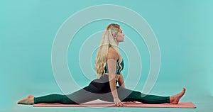 Fitness, woman and yoga splits stretching body on mat for workout, exercise or training against a blue studio background