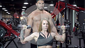 Fitness woman and young trainer man are exercising muscles with dumbbells in gym.