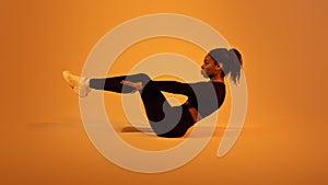 Fitness workout. Active black lady doing abs exercises lying on floor over orange neon studio background, side view