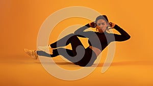 Fitness workout. Black sportswoman in fitwear doing elbow to knee abs crunch exercising on neon orange sudio background
