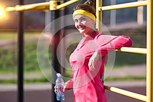 Fitness and Workout Concepts. Happy Smiling Caucasian Female Athlete in Professional Outfit Posing With Water Bottle Near trainer