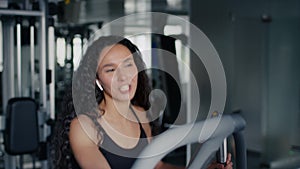 Fitness workout at gym. Young lady athlete listening to music via wireless earphones, exercising on training apparatus