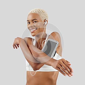 Fitness workout, happy smiling woman stretching arms wears earphones of mobile phone on arm band, african latin american athlete