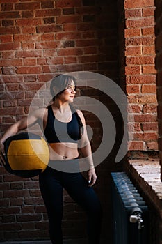 Fitness young athletic woman with strong beautiful body in black sportswear posing with heavy medicine ball having