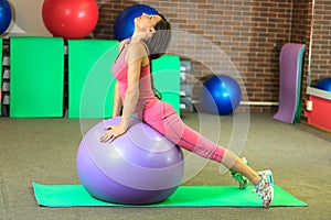 Fitness. Young beautiful white girl in a pink sports suit does physical exercises with a violet fit ball at the fitness center.