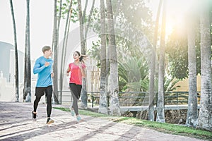 Fitness young couple running outdoor with palms in background - Sporty happy people training in tropical place - Healthy lifestyle