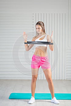 Fitness young woman doing back exercise with resistance band for training strength. Female athete exercising