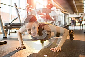 Fitness young woman doing push ups and looking at camera at gym