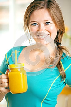 Fitness young woman drinking orange smoothie in Kitchen