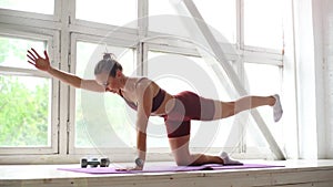 Fitness young woman with perfect athletic body in sportswear doing stretching exercises at window sill during workout