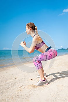 Fitness young woman working out core and glutes with bodyweight workout doing squat exercises on beach