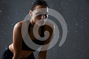 Fitnesswoman holding hands on knees under rain.