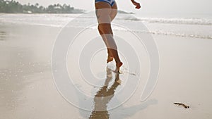 Fitted female feet running barefoot, making water splashes at sea water waves. Woman's legs leaving footprints on