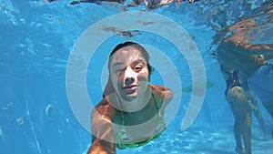 Fitted pretty woman in swimsuit diving under water in swimming pool, shooting herself on action camera. Mixed race girl