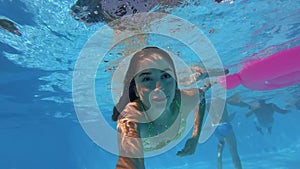 Fitted pretty woman in swimsuit diving under water in swimming pool, shooting herself on action camera. Mixed race girl