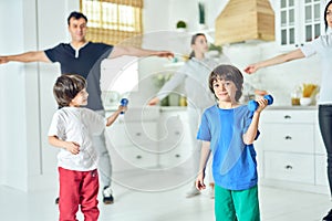 Fitter, healthier, happier. Cute little latin boy smiling at camera, exercising with dumbbell while working out together
