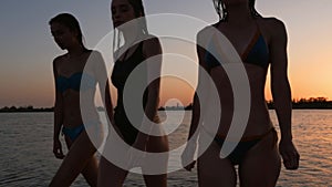 Fittted slim pretty girls silhouettes in bikini walking out of water after bathing in sea on sunset. Women in swimsuits