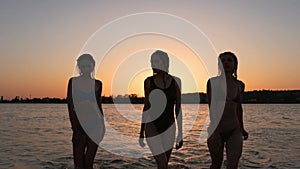 Fittted slim pretty girls silhouettes in bikini walking out of water after bathing in sea on sunset. Women in swimsuits