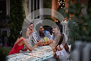 Group of five adults making toast with cocktails, at the outdoor bar, laughing, having fun. Fun, party, socializing, multiethnic, photo