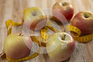 Five apples surrounded by a tape measure and on weathered wood background