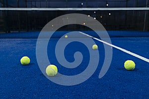 Five balls on a blue paddle tennis court at dusk, racket sports concept