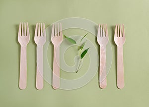 Five bamboo wood forks with a plant lie in a row on a green background. No plastic concept.