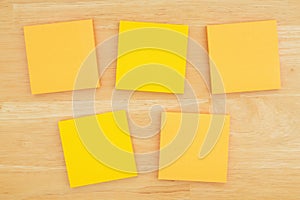 Five blank sticky notes on textured desk wood background