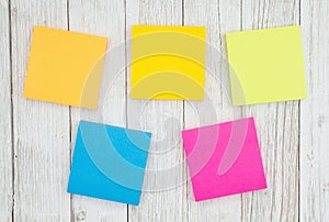 Five blank sticky notes on weathered whitewash textured wood background