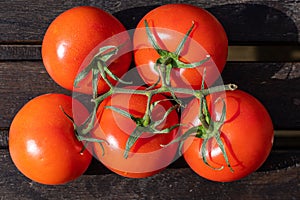 Five bright red freshly picked tomatoes with leaves and stem on dark brown rustic wooden table