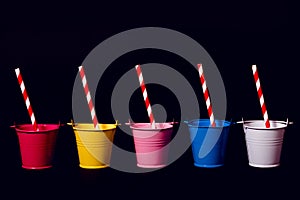 Five buckets against a black background with striped red and white straws