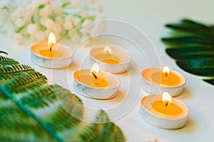 Five burning candles with small bouquet and green leaves on white background. Relaxation and aromatherapy concept