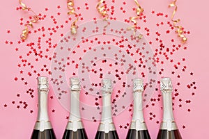 Five Champagne bottles with confetti stars and party streamers on pink background. Copy space,top view. Party background
