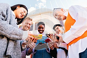 Five cherful friends using his cellphone and having fun together. Low angle of multiethnic group of happy people sharing