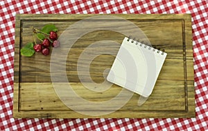 Five cherries with leaves in corner of wooden board and paper for recipe