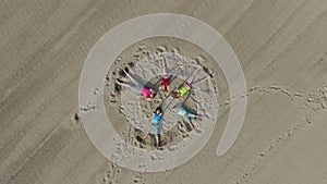 Five children lie on the sand in the shape of a star and wave their hands