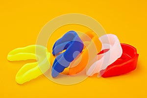 Five colored boxing mouth guards laid out in a row on a yellow background, concept photo