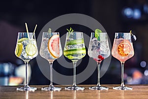 Five colorful gin tonic cocktails in wine glasses on bar counter