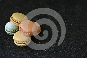 Five colorful macaroons in a pile on a black background. Five tasty cookies